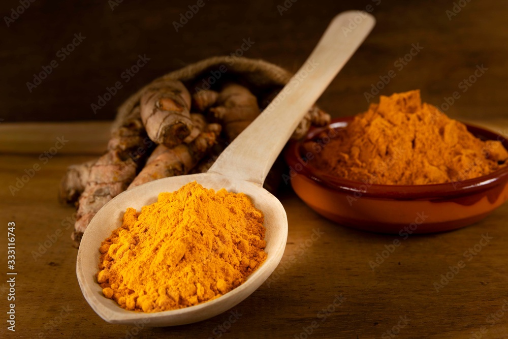 Turmeric powder and roots on a dark wooden surface Turmeric powder and roots on a dark wooden surface