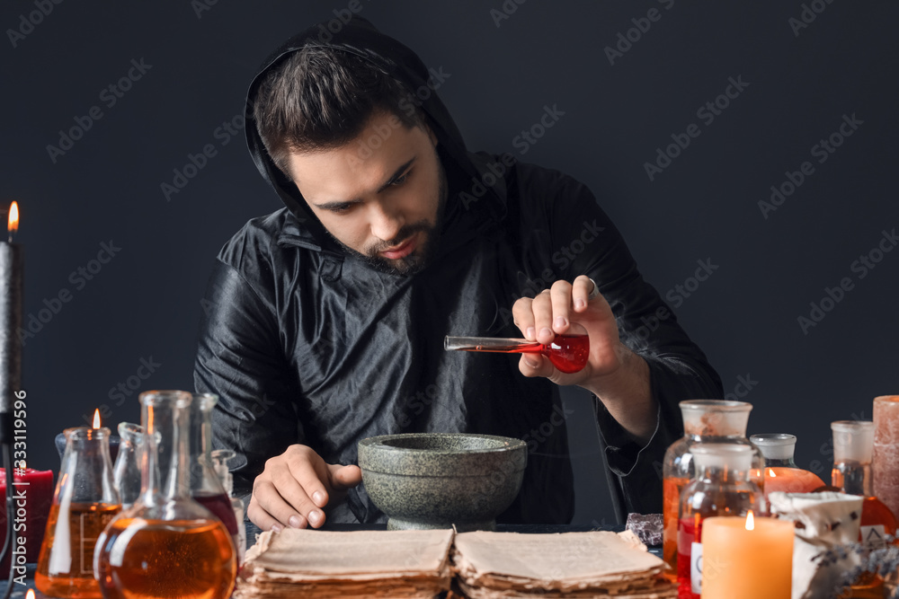 Male alchemist making potion on dark background Male alchemist making potion on dark background