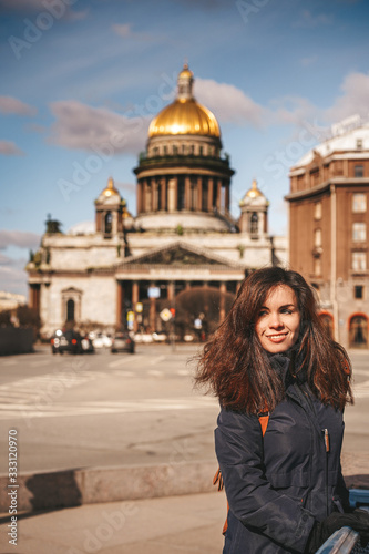 Brunette girl in jacket with fur hood is in the opposite direction from the camera and looking at St. Isaac's Cathedral and the main square in Saint-Petersburg Russia