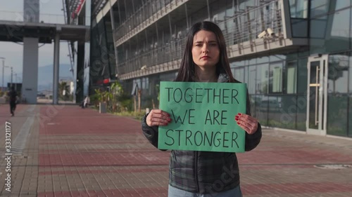 A young woman stands on the street and holds a poster with the inscription 