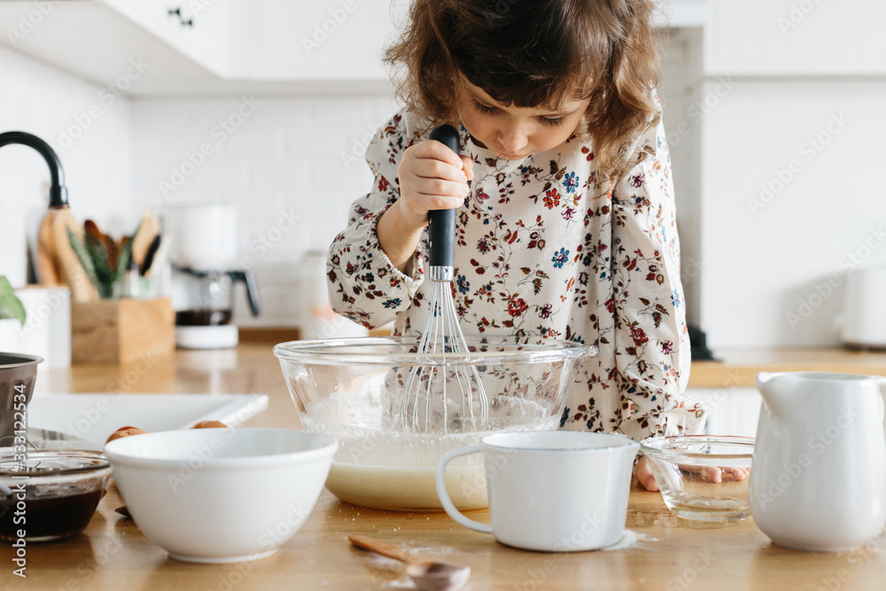 Cute 5 years girl wearing dress preparing cake at the white modern kitchen. Cute 5 years girl wearing dress preparing cake at the white modern kitchen.