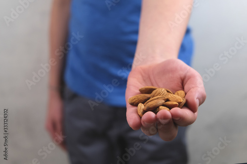 Almonds nuts in a child's hand in a blue T-shirt and gray pants close-up on a white blurred background. Side view.