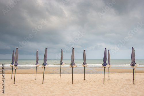Many umbrellas on the sandy beach Background sea and black rain clouds.
