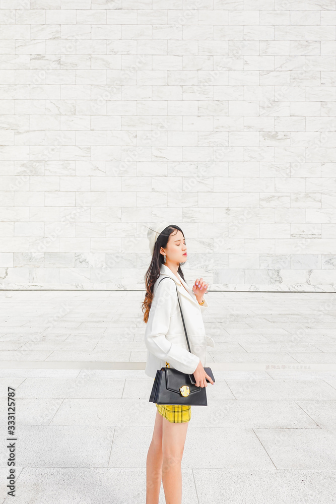 Portrait of beautiful young asian woman standing against big white wall