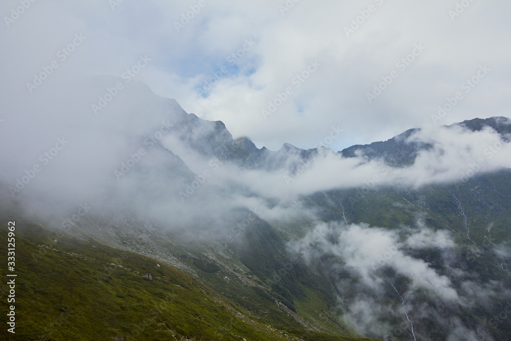 Majestic landscape of summer mountains. View of rocky peaks and coniferous forest hills in fog. Fagaras Mountains.Transylvania. Romania. Wild nature relaxing background. Majestic landscape of summer mountains. View of rocky peaks and coniferous forest hills in fog. Fagaras Mountains.Transylvania. Romania. Wild nature relaxing background.