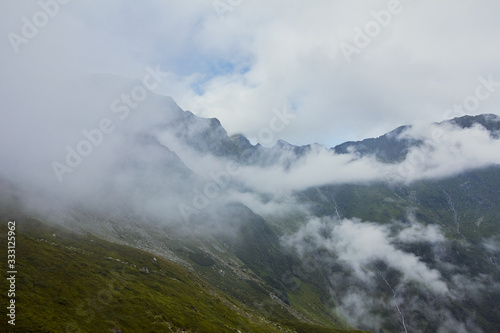Majestic landscape of summer mountains. View of rocky peaks and coniferous forest hills in fog. Fagaras Mountains.Transylvania. Romania. Wild nature relaxing background. © vovik_mar