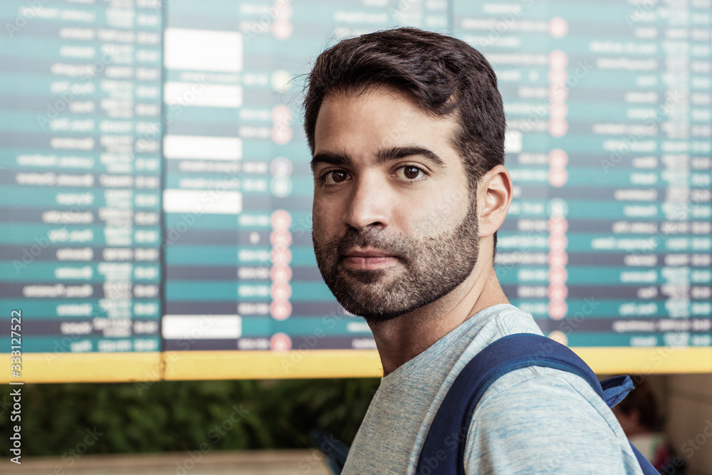 Serious Hispanic man posing near departure board. Focused bearded guy looking at camera. Travel concept