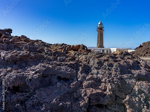 In the foreground volcanic rock, a very common landscape on the coast of the island of El Hierro.  In the background, out of focus is the La Orchilla Lighthouse. © AventurasxCanarias