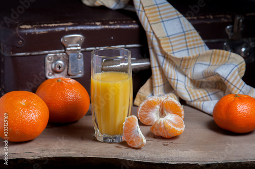 Unpeeled round ripe orange mandarins or tangerines, slices of peeled mandarin and glass of fresh juice on wooden board.