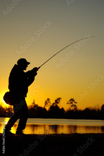 A fisherman silhouette fighting a bass fish at sunset