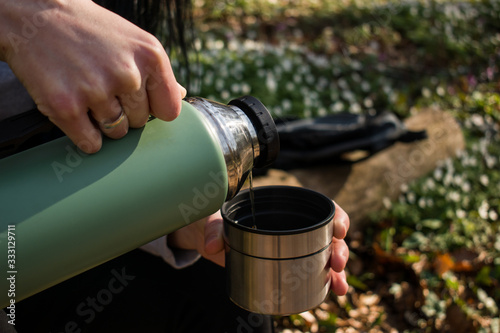 Close up hands pouring tea, coffee in a cup, mug from thermos bottle outdoor in the forest. People and healthy lifestyle concept