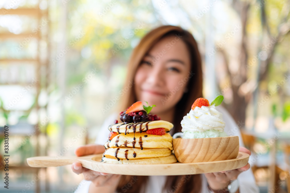 A beautiful asian woman holding and showing a plate of pancakes with ice cream and whipped cream in cafe