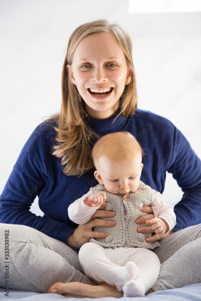 Happy overjoyed new mom enjoying time with cute little baby girl. Young woman nursing six month daughter in bedroom at home. Motherhood concept Happy overjoyed new mom enjoying time with cute little baby girl. Young woman nursing six month daughter in bedroom at home. Motherhood concept