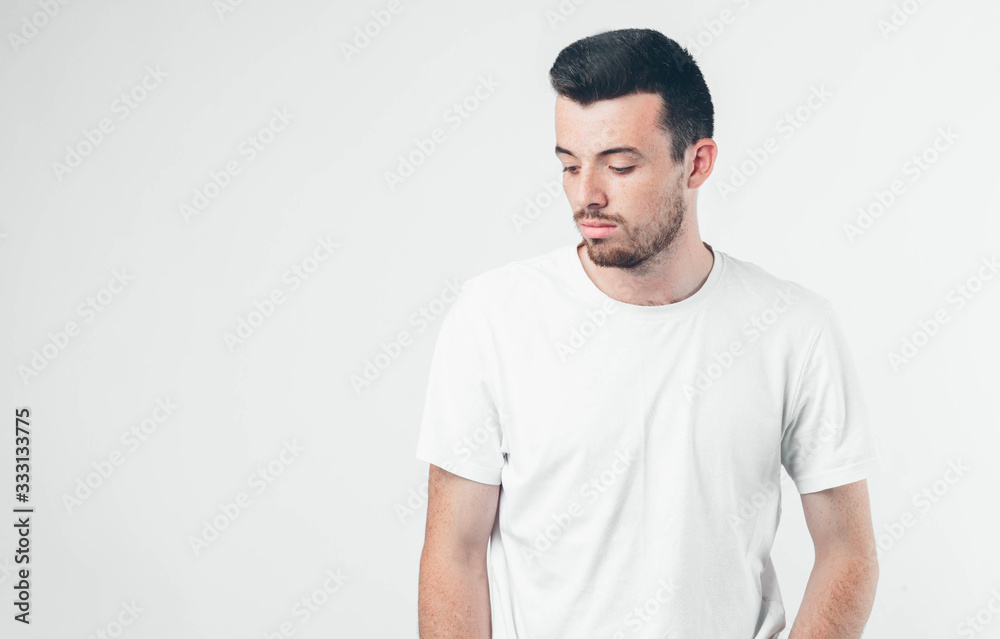 Young brunette man with beard dressed in white T-shirt. Guy with serious and concentrated face. His hands down. Isolated over light background. Young brunette man with beard dressed in white T-shirt. Guy with serious and concentrated face. His hands down. Isolated over light background.