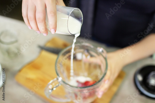 A female hand pours milk into a blender to prepare a tasty and healthy smoothie of strawberries and almond.