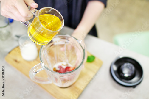 A female hand pours tea into a blender to prepare a tasty and healthy smoothie of strawberries and almond.