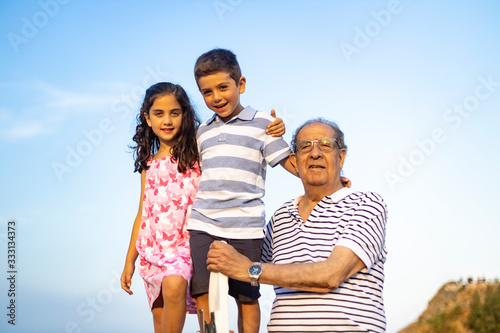 Grandfather and grandchildren against blue sky. Summer time.