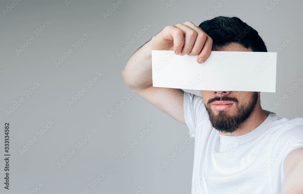 Young man isolated over background. Side view and selfie of bearded guy  hide eyes from camera. Hold iece of paper or page in hand. Stock Photo |  Adobe Stock