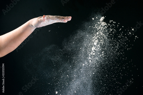 Isolated on black background female hand pours white flour like snow for baking © Niko_Dali
