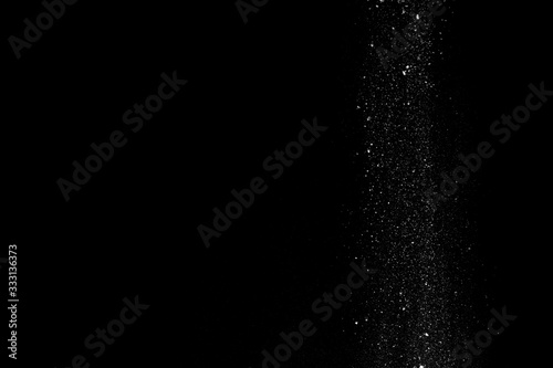 White powder in the form of snow or flour falls from top to bottom isolated on black background
