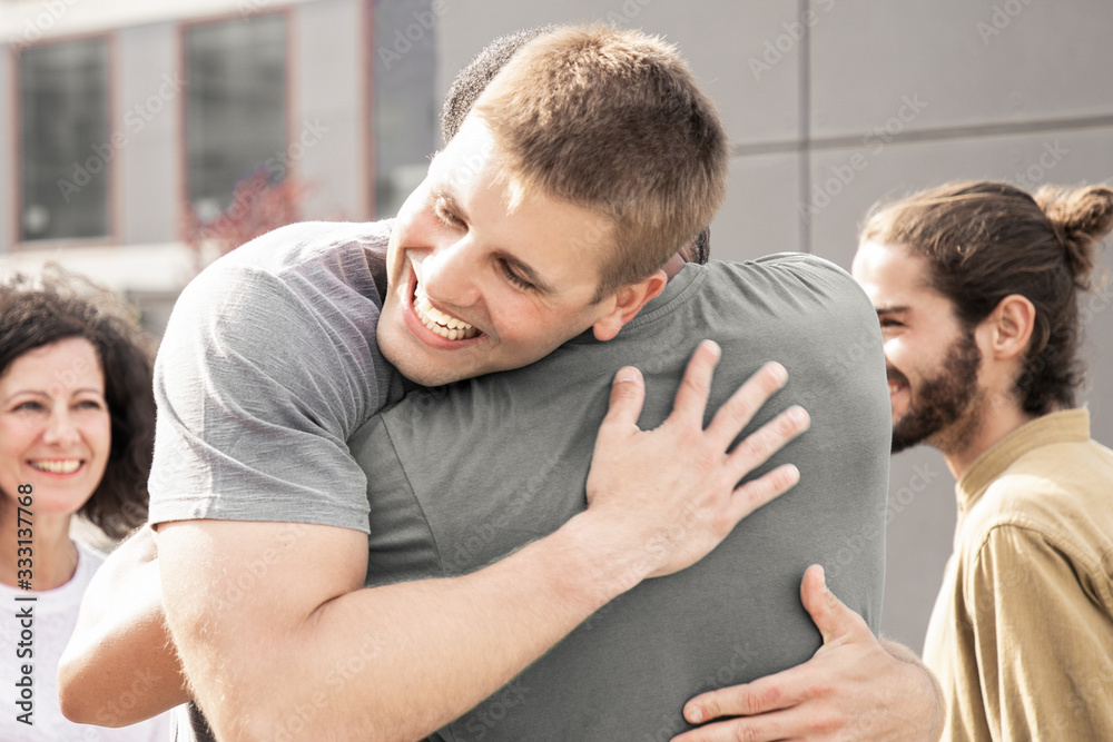 Fototapeta premium Multiethnic friends greeting each other. Happy young men and women smiling and hugging on street. Friendship concept