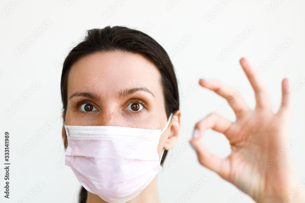 white caucasian woman wearing medical mask looking at camera on white background wall making ok sign with her fingers white caucasian woman wearing medical mask looking at camera on white background wall making ok sign with her fingers