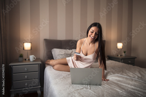 Girl sitting on the bed and buying online with her credit card.