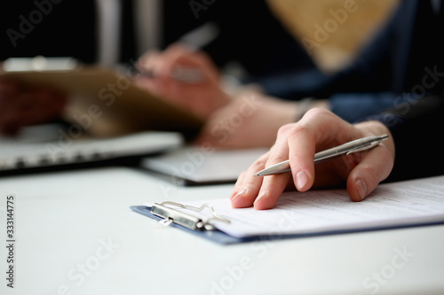 Photography Hand of businessman in suit filling and signing with silver pen partnership agreement form clipped to pad closeup