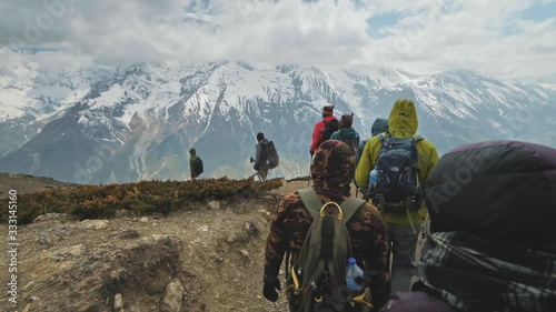 Tourist expedition trekking down in mountains next to giant snow massif in cloud