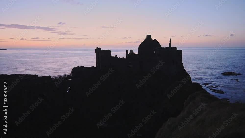 The Profile Of Dunluce Castle And The Coast Of Antrim And Glens During Sunset In Antrim County, Northern Ireland. -wide shot The Profile Of Dunluce Castle And The Coast Of Antrim And Glens During Sunset In Antrim County, Northern Ireland. -wide shot