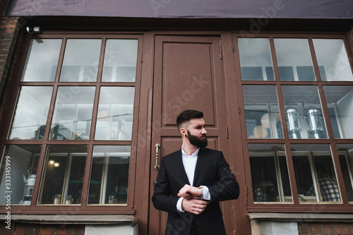 A young handsome man with a beard in a business suit stands on the street of the city.