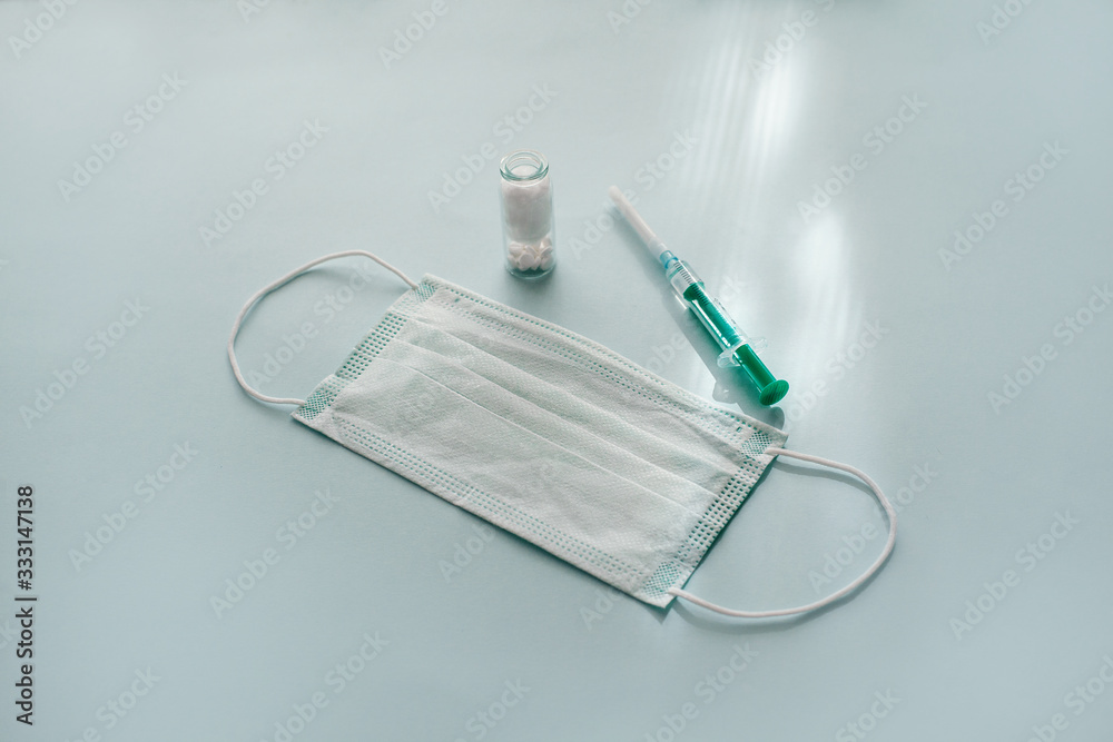 A protective mask, a green syringe and a bottle of pills on a blue background. Concept of health protection and prevention of viral diseases. The view from the top, place for text A protective mask, a green syringe and a bottle of pills on a blue background. Concept of health protection and prevention of viral diseases. The view from the top, place for text