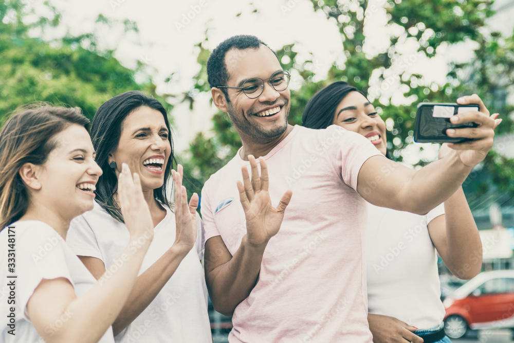 Smiling friends waving to camera phone. Group of cheerful young people posing for selfie. Concept of self portrait Smiling friends waving to camera phone. Group of cheerful young people posing for selfie. Concept of self portrait