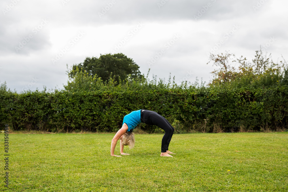 A middle aged woman practicing yoga barefoot outside in a grassy park A middle aged woman practicing yoga barefoot outside in a grassy park
