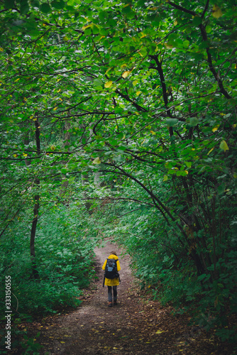 Hiker girl on a trail in the forest wearing yellow jacket and backpack © Kudar