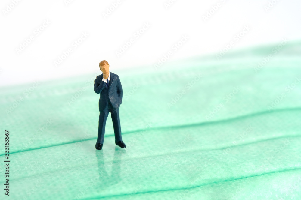 Miniature people photography - a businessman stands above green face mask