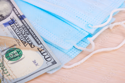 Medical blue masks and one banknote of 100 dollars,lying on light background.Soft focus.Concept of protection, deficiency, high cost of remedies for epidemics,pandemics,coronavirus, bacterial infectio photo