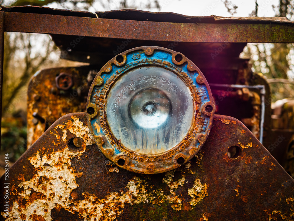 Dilapidated, run down train carriage, taken close up with focus on the headlight. Train is Covered in rust and patina, and in a remote countryside area.