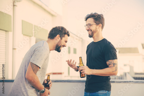 Two male friends drinking beer and sharing funny news on outdoor terrace. Two young men in casual meeting outside. Friendly chatting concept