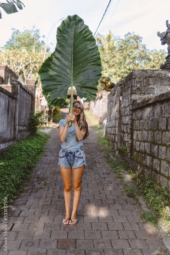 Beautiful and young slender girl poses as a model with a leaf on the island of Bali. The culture and nature of a tropical island is conveyed. Emotions and happiness Beautiful and young slender girl poses as a model with a leaf on the island of Bali. The culture and nature of a tropical island is conveyed. Emotions and happiness
