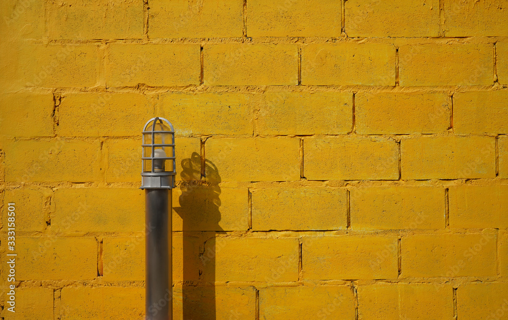 An electric light metal pole is in front of yellow wall. Row of brick works are built horizontally. Home decoration, renovation, background, textures and object ideas. An electric light metal pole is in front of yellow wall. Row of brick works are built horizontally. Home decoration, renovation, background, textures and object ideas.