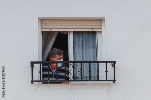 Man with a mask confined in quarantine to prevent coronavirus spread to the window. photo