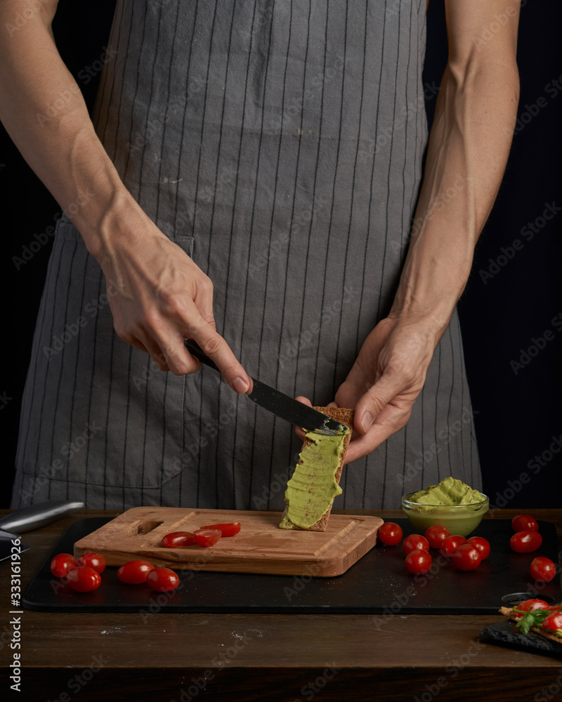 Chef man hands on cook appetizer sandwiches with guacamole and tomatoes. healthy breakfast food, vegetarian food, diet. Gark style photo. Chef man hands on cook appetizer sandwiches with guacamole and tomatoes. healthy breakfast food, vegetarian food, diet. Gark style photo.