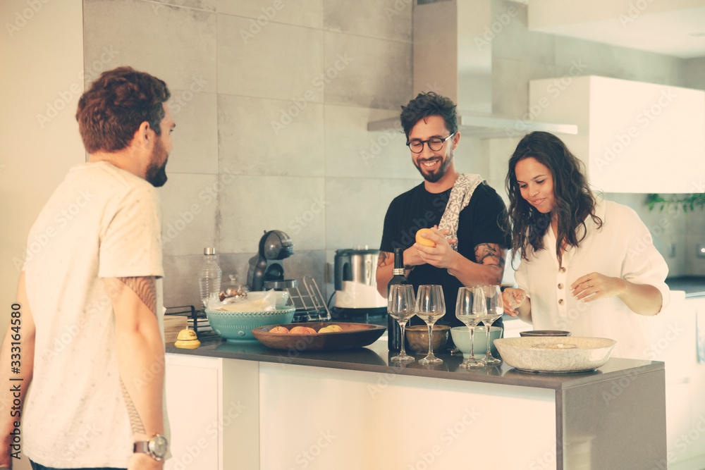 Obraz premium Happy couple cooking dinner for friends together in kitchen. Young men and women in casual meeting indoors. Cooking at home concept