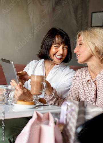 Two mature women chatting and using the tablet device while having lunch in cafe