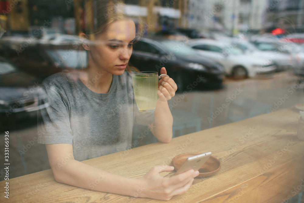 Fototapeta premium The blonde uses the phone. Girl and smartphone. A woman is sitting in a cafe with a cellular