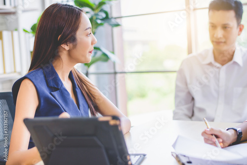 Attractive young Asian Business woman presenting and discussing financial data and analyzing report graph by digital tablet at office. Teamwork meeting and partnership conference working concept.