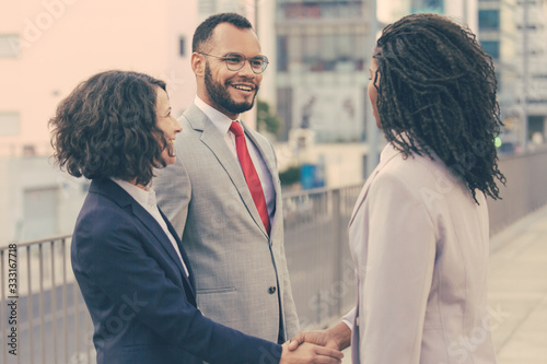 Friendly business partners discussing deal outside. Business man and women standing near city building, shaking hands, smiling and talking. Agreement concept