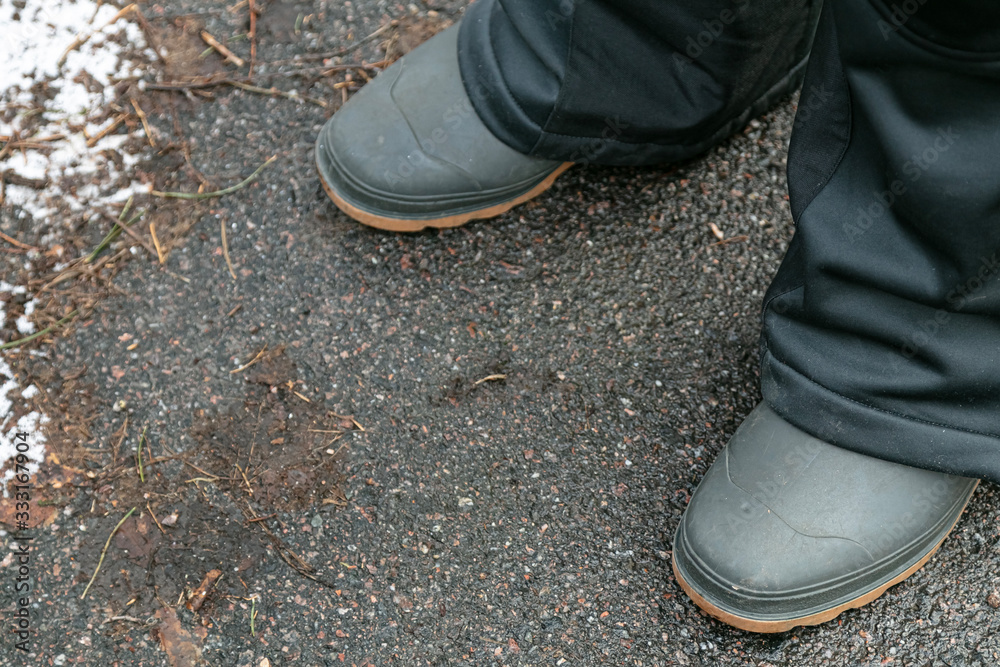 Rubber boots on the pavement. Close-up of the legs in rubber boots. The man. Rubber boots on the pavement. Close-up of the legs in rubber boots. The man.