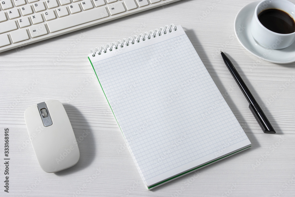 An empty Notepad next to a mouse, keyboard, and a white coffee Cup on a white office Desk, side view An empty Notepad next to a mouse, keyboard, and a white coffee Cup on a white office Desk, side view